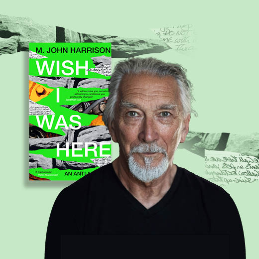 A photo of M. John Harrison, an older white man with white hair pulled back into a ponytail and a white goatee. He is on a light green background with the book 'Wish I Was Here' behind him.