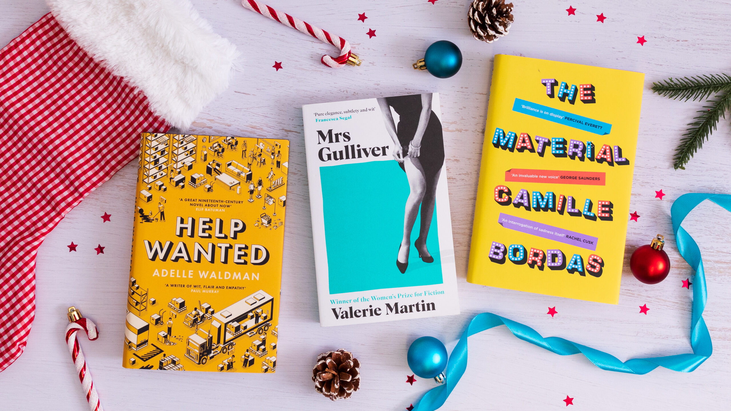 A top-down photograph featuring four Serpent's Tail books with Christmas decorations surrounding them. The books are: The Material, Mrs Gulliver and Help Wanted.